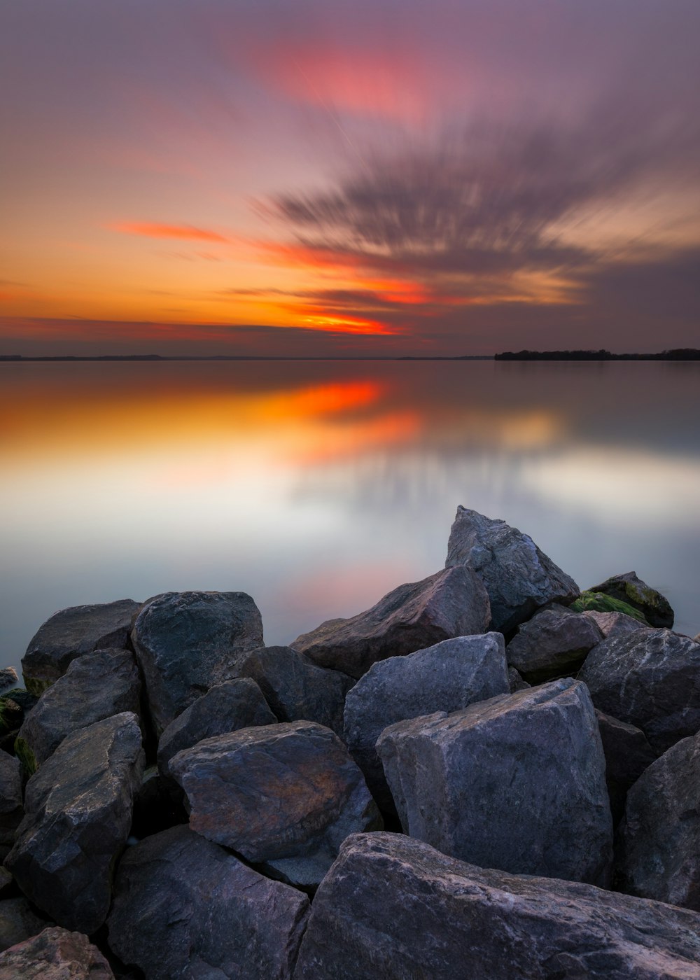 a sunset over a body of water with rocks in the foreground