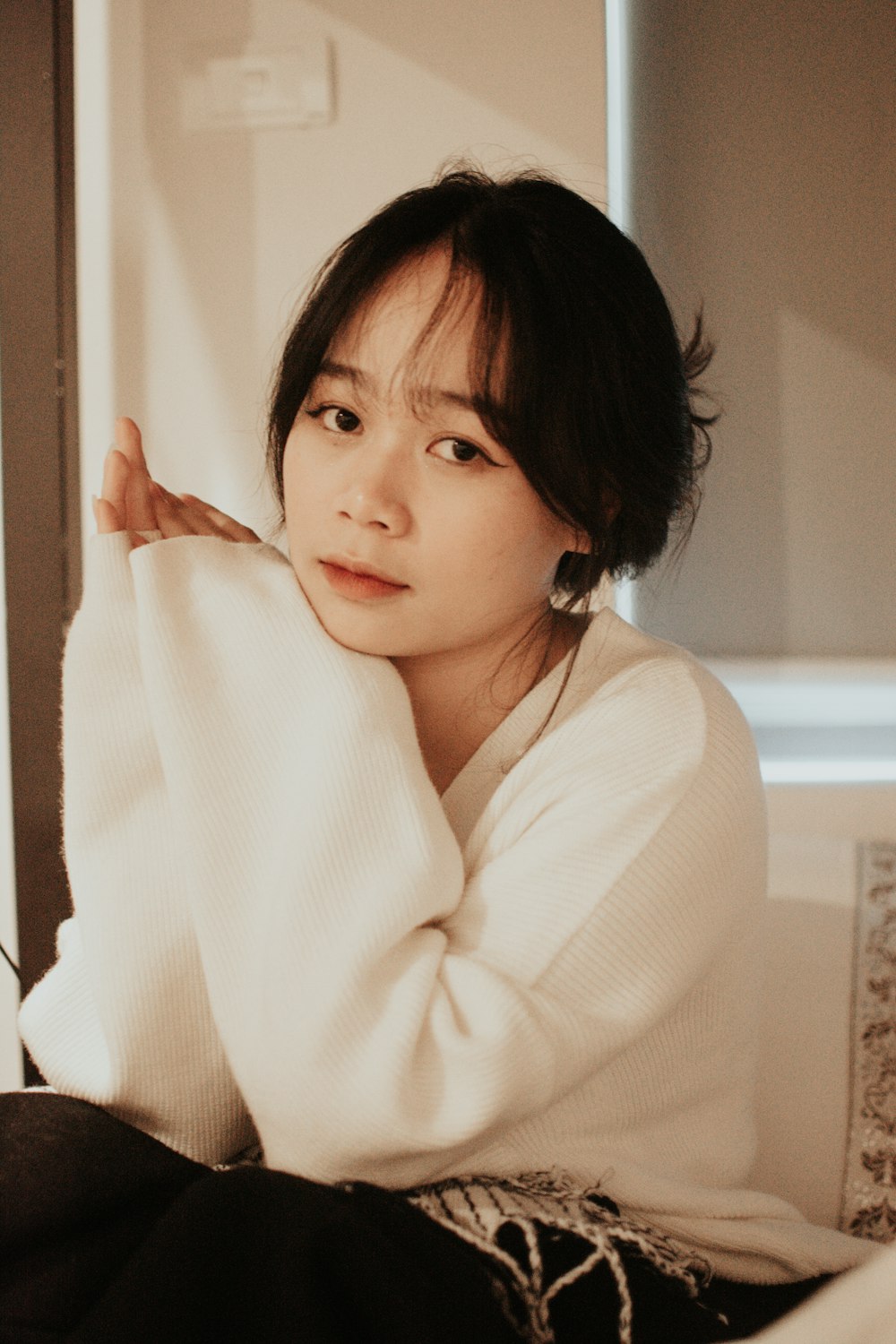 a woman sitting on a bed in a white sweater