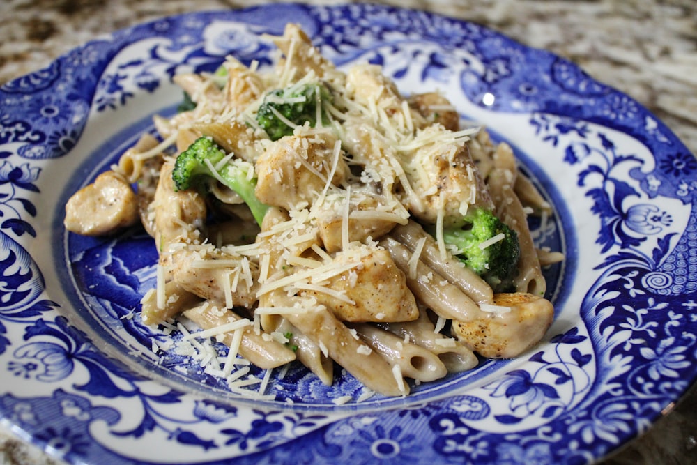 a blue and white plate topped with pasta and broccoli