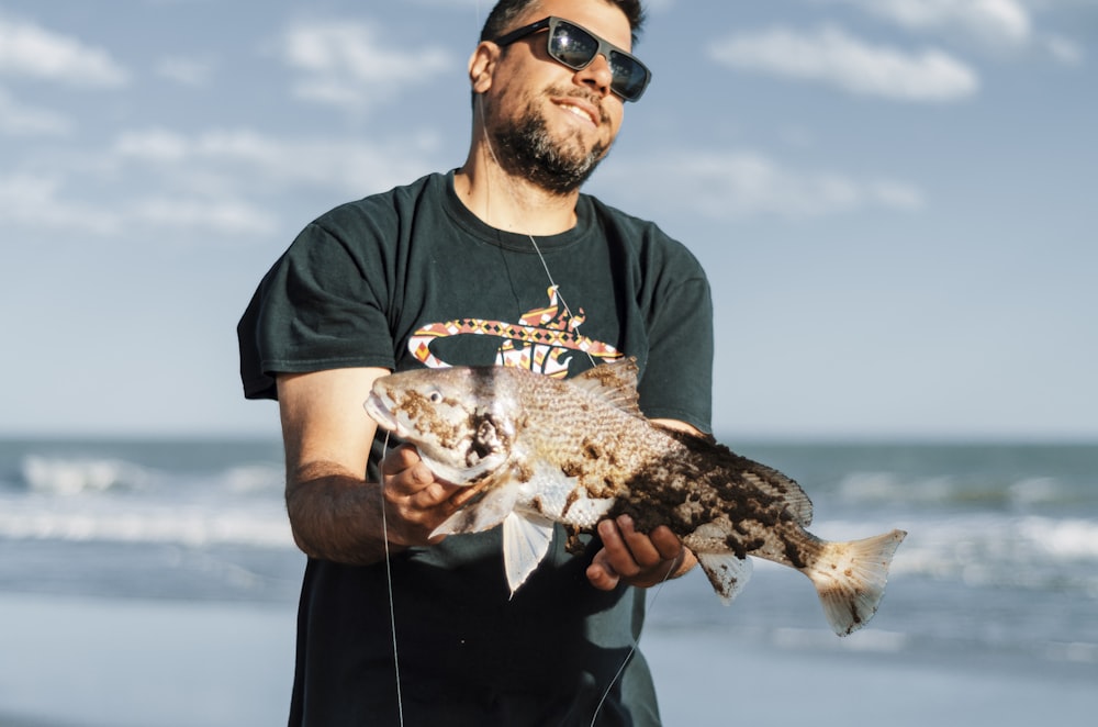 a man holding a fish on the beach