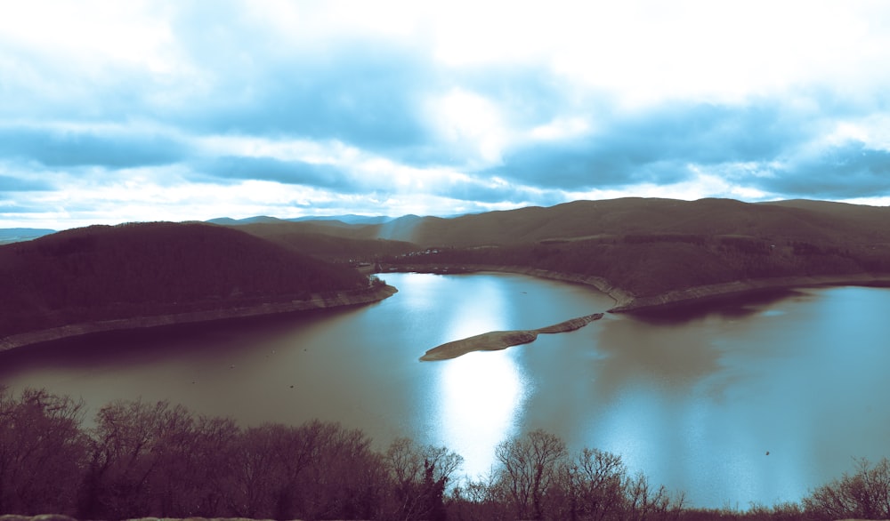 a lake surrounded by mountains under a cloudy sky