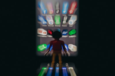 A blurred toy figure stands facing a smartphone screen filled with app icons, creating a surreal effect. The apps appear stretched and give a sense of being drawn towards the screen.