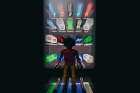 A blurred toy figure stands facing a smartphone screen filled with app icons, creating a surreal effect. The apps appear stretched and give a sense of being drawn towards the screen.