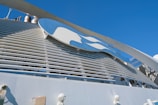 A large structure featuring a prominent logo with a blue and white color scheme is set against a clear blue sky. The design includes a stylized profile of a person with flowing hair. The image also includes industrial elements such as pipes and vents.