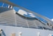 A large structure featuring a prominent logo with a blue and white color scheme is set against a clear blue sky. The design includes a stylized profile of a person with flowing hair. The image also includes industrial elements such as pipes and vents.