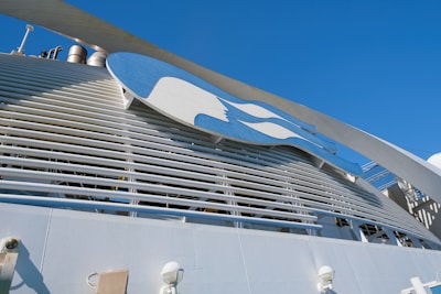 A large structure featuring a prominent logo with a blue and white color scheme is set against a clear blue sky. The design includes a stylized profile of a person with flowing hair. The image also includes industrial elements such as pipes and vents.
