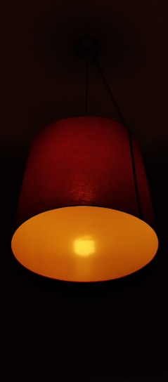 A sleek red therapy lamp glowing softly in a dark, cozy bedroom setting.