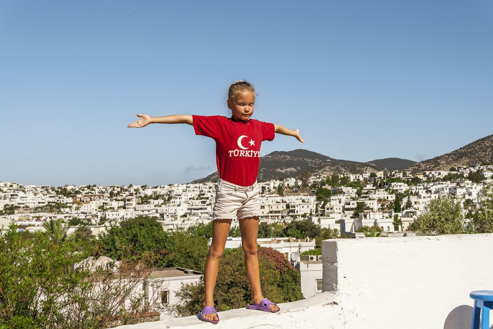 a little girl standing on a ledge with her arms outstretched