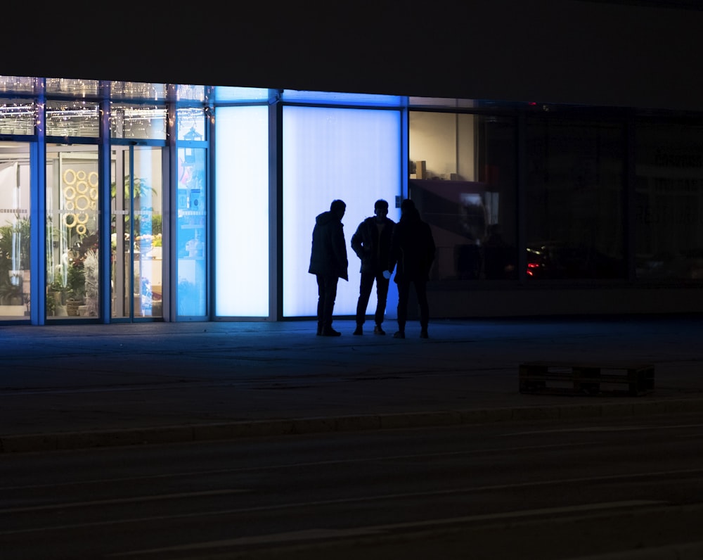 três pessoas em pé em frente a um prédio à noite