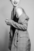 A person is stylishly dressed in a checkered jacket, smiling slightly with a confident pose. The image is in black and white, giving it a classic and elegant feel.