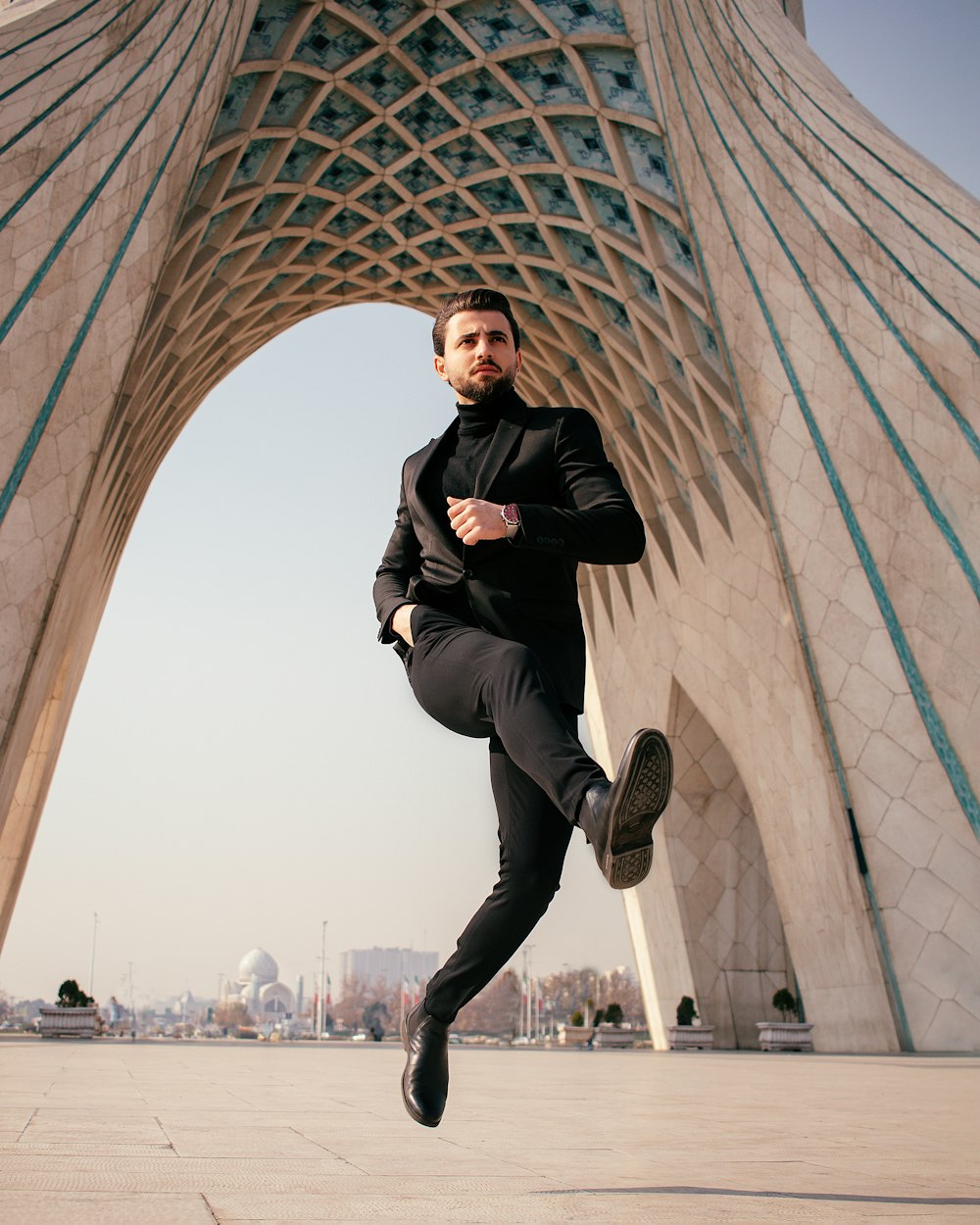 a man in a black suit is posing in front of a building