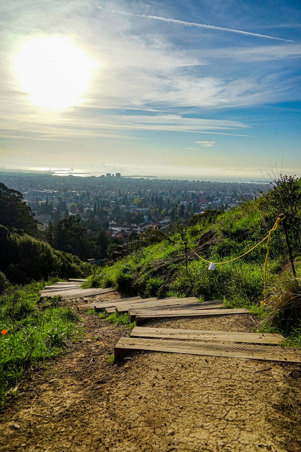 a wooden path going up a hill with a view of a city in the distance
