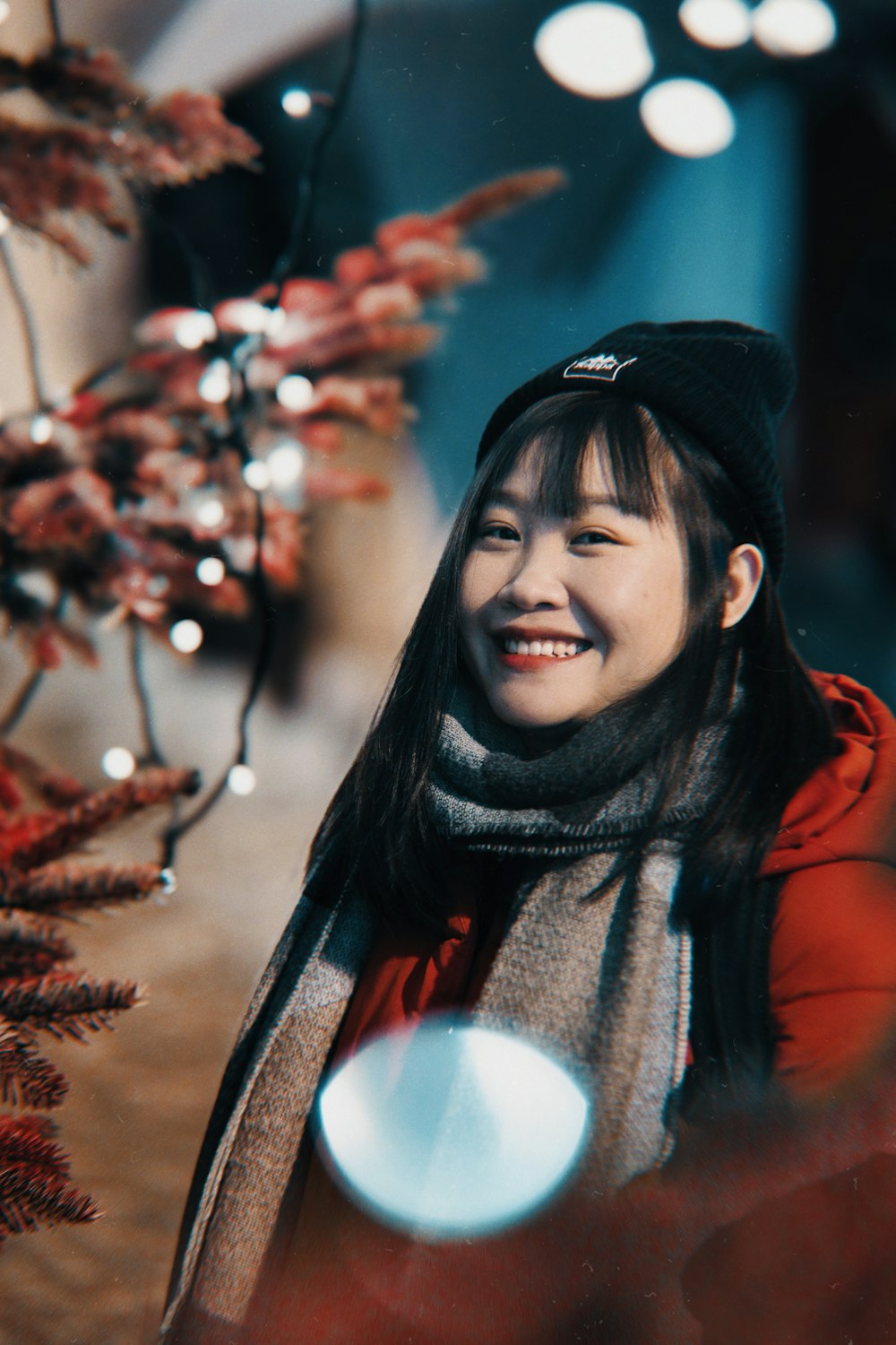 a woman smiles while standing next to a christmas tree