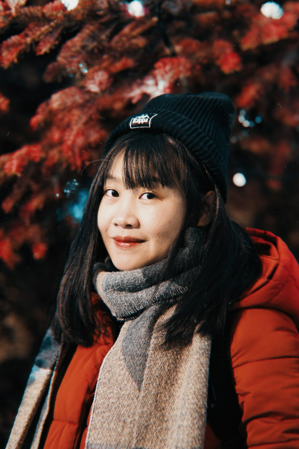 a woman wearing a hat and scarf standing in front of a tree