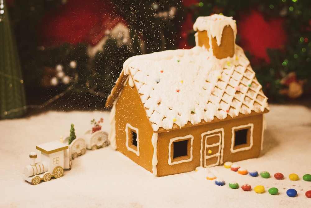 a gingerbread house with a train and a christmas tree in the background