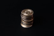 A stack of gold crypto coins with intricate patterns and symbols against a dark background, illuminated to highlight their metallic luster.