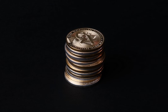 A stack of gold crypto coins with intricate patterns and symbols against a dark background, illuminated to highlight their metallic luster.