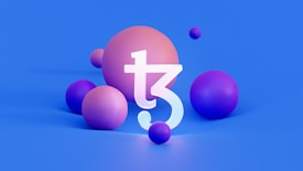 A large three-dimensional 'T' symbol is centered among several spherical objects varying in size. The background is a solid blue while the spheres are shades of pink and purple. The symbol appears to be white with a slight glow.