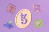 A 3D illustration featuring a large coin with a stylized symbol in the center surrounded by various floating icons. These include a letter T on a square background, an image icon, a play button, and a virtual reality headset. The background is a soft purple hue.