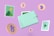 A stylized image features a pastel-colored wallet surrounded by symbols of digital currency, such as Bitcoin and Tezos icons. There are also illustrative graphics resembling mountains and a play button. The background is a solid lavender color, complementing the soft tones of the design.