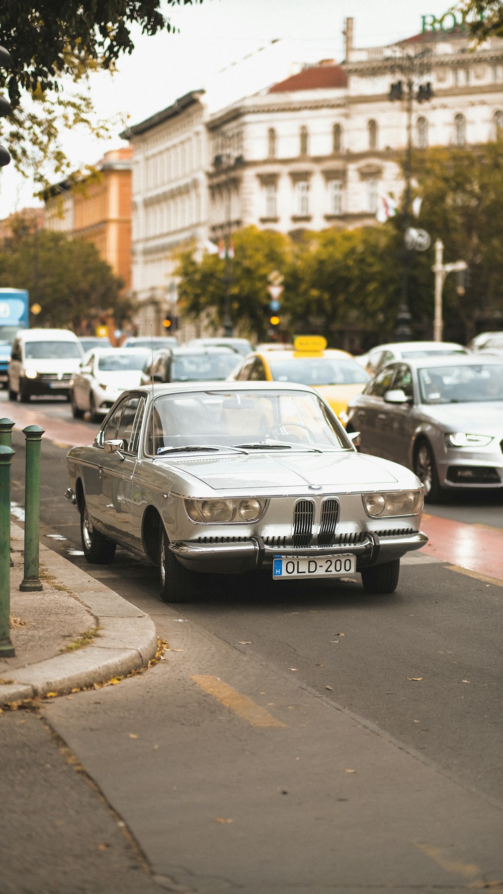 a silver car driving down a street next to tall buildings