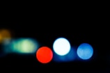 A dark background with several unfocused, blurry colored circles resembling bokeh lights. The colors include red, light blue, and green, creating a soft, dreamy effect.