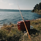 An angler packing a tackle box beside a calm lake at sunrise.