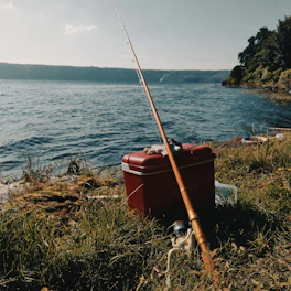 A cozy lakeside setup with a fishing rod, cooler, and sunhat resting on a wooden dock.