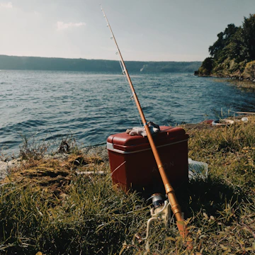 A cozy lakeside setup with a fishing rod, cooler, and sunhat resting on a wooden dock.