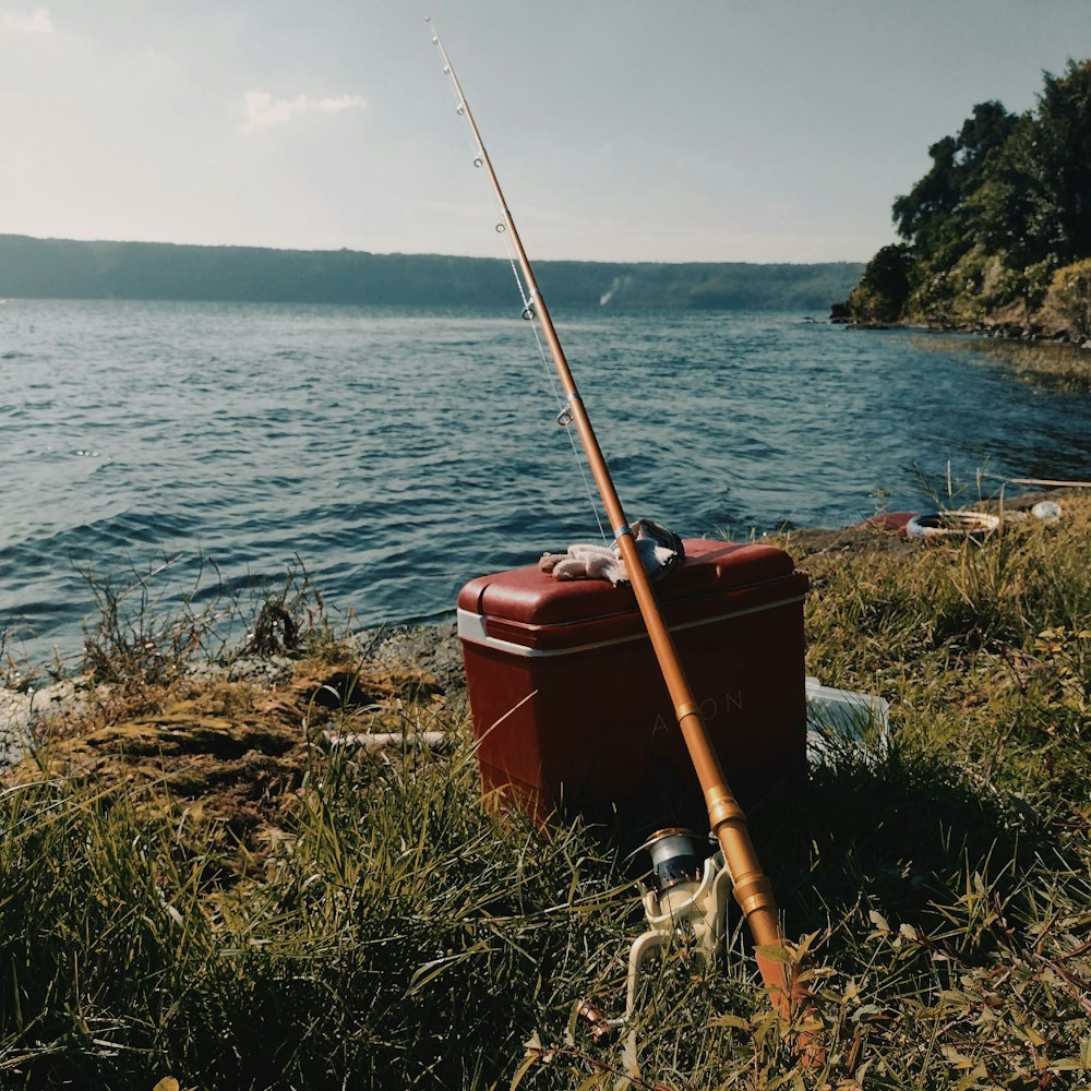a fishing rod sitting on top of a red box next to a body of water