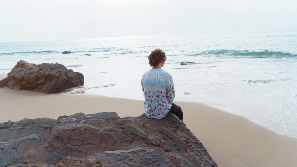 a man sitting on a rock looking out at the ocean