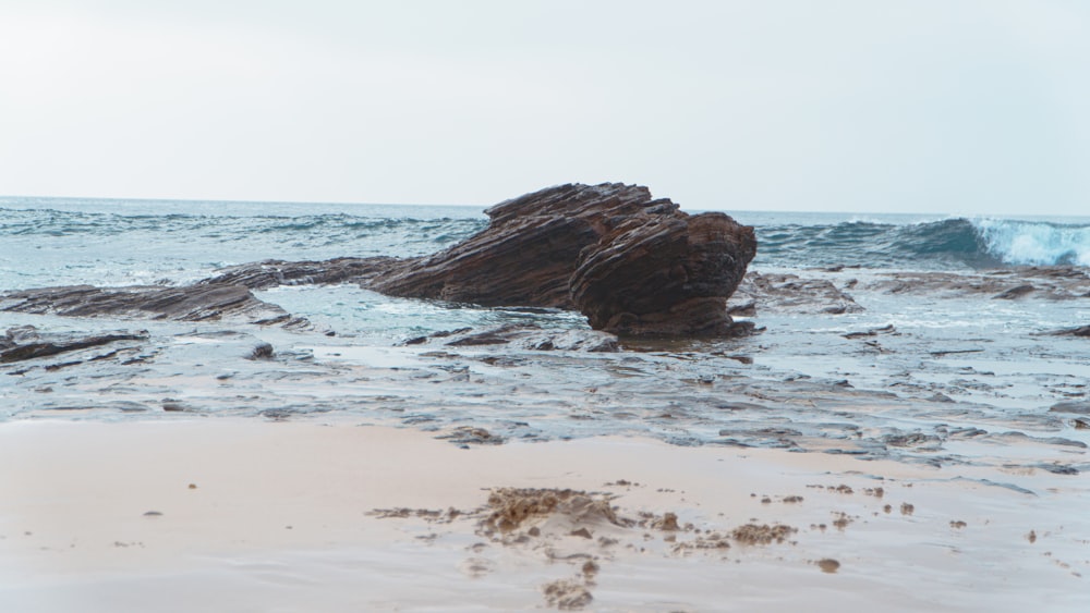 a rock sticking out of the water on a beach