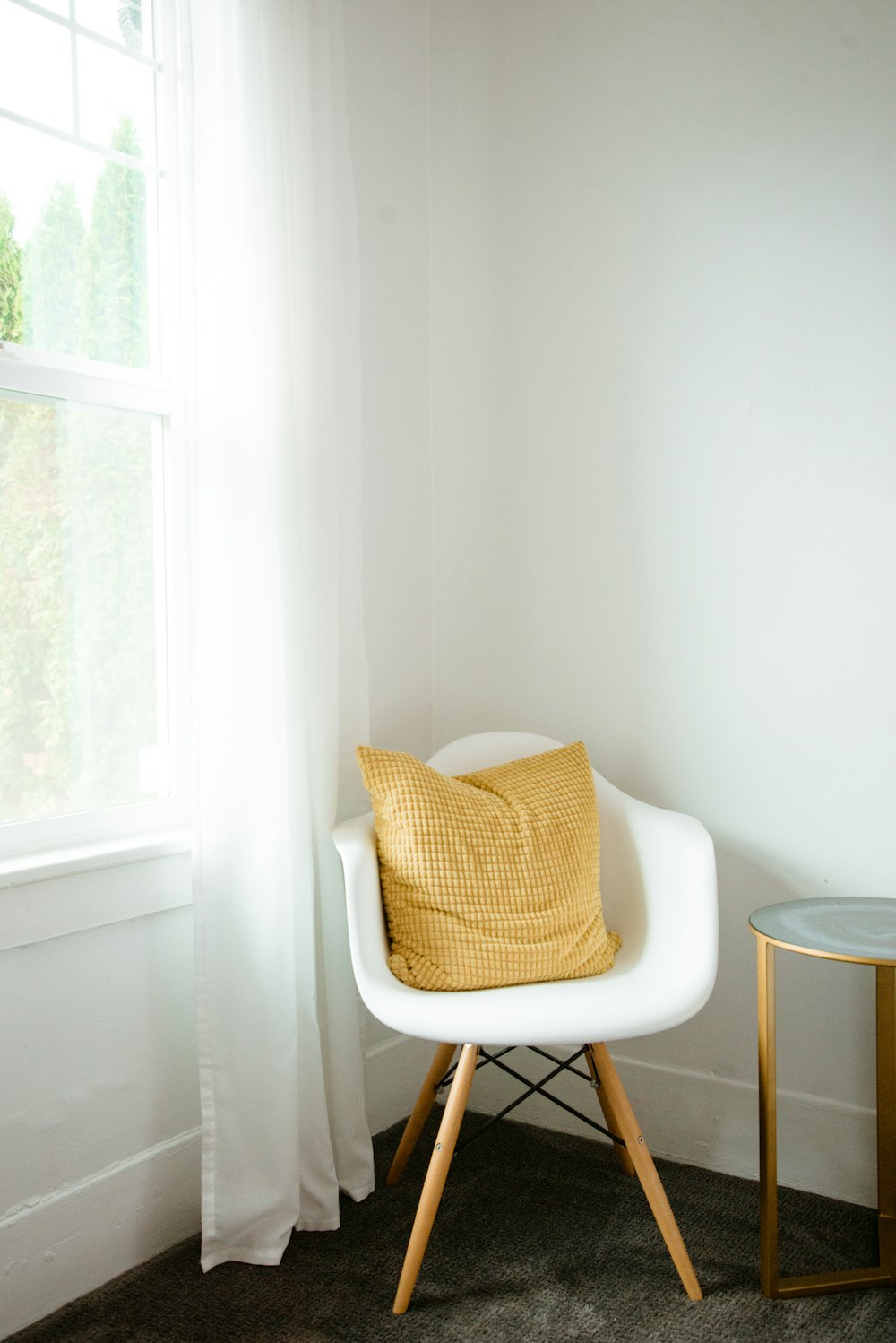 a white chair with a yellow pillow next to a window