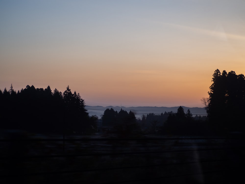 the sun is setting over the trees on the side of the road