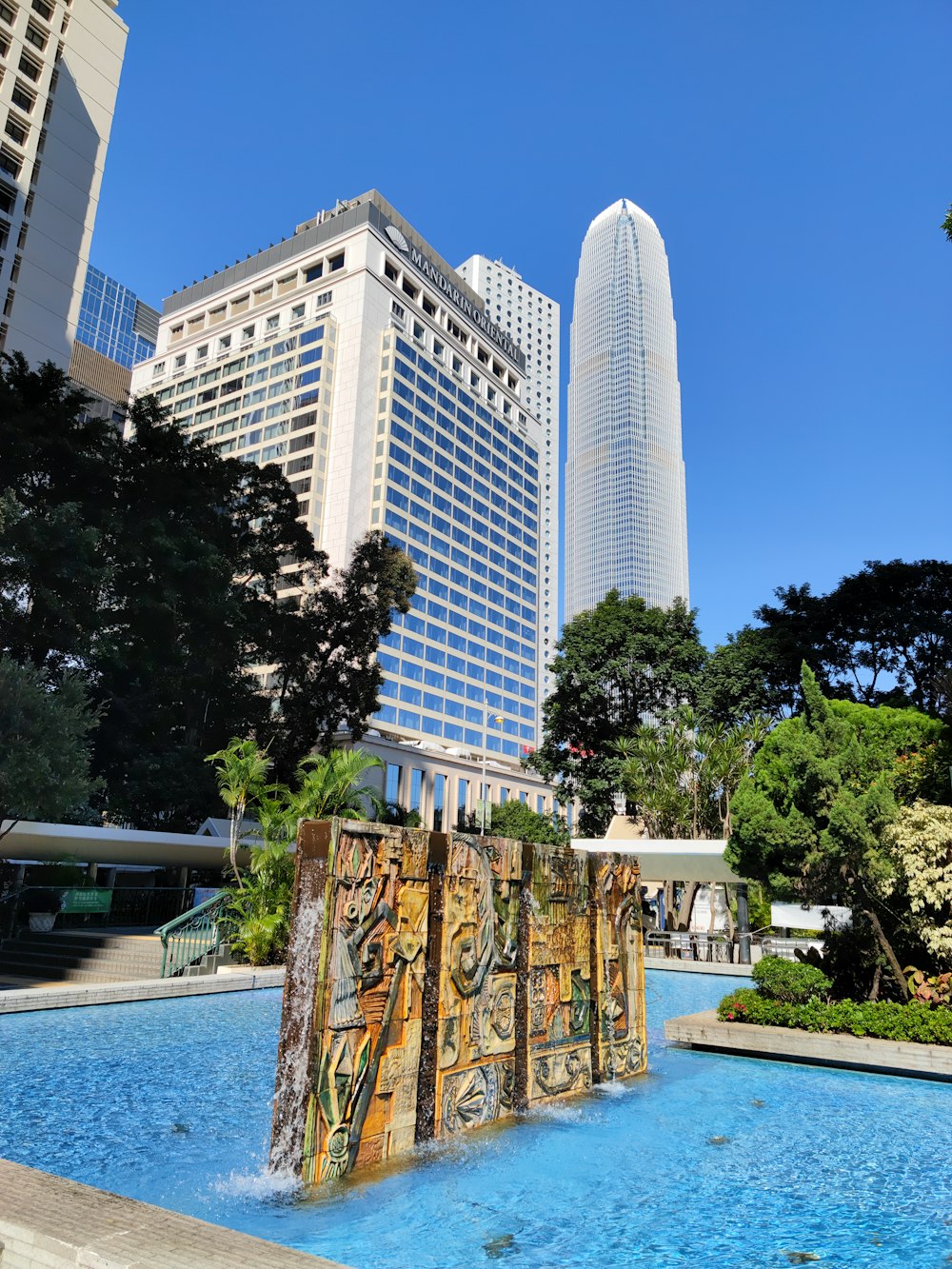 a fountain in the middle of a park with tall buildings in the background