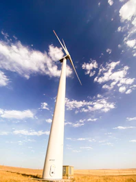 A compact wind turbine standing tall on a green farm field under a clear blue sky.