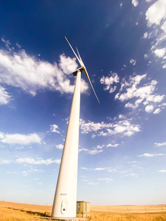 A compact wind turbine standing tall on a green farm field under a clear blue sky.