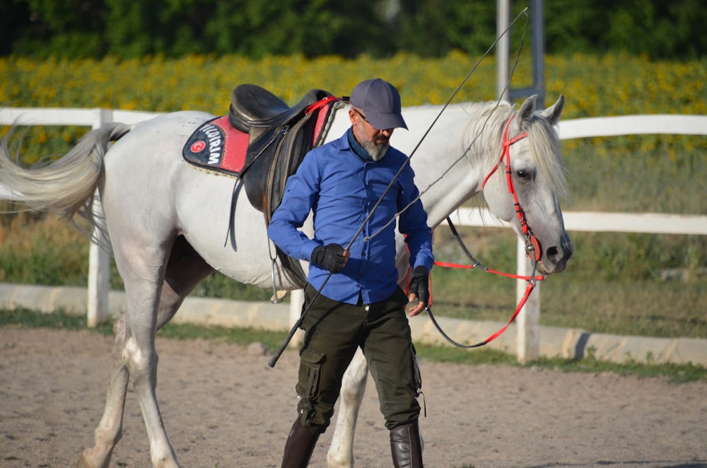 a man in a blue jacket is walking a white horse