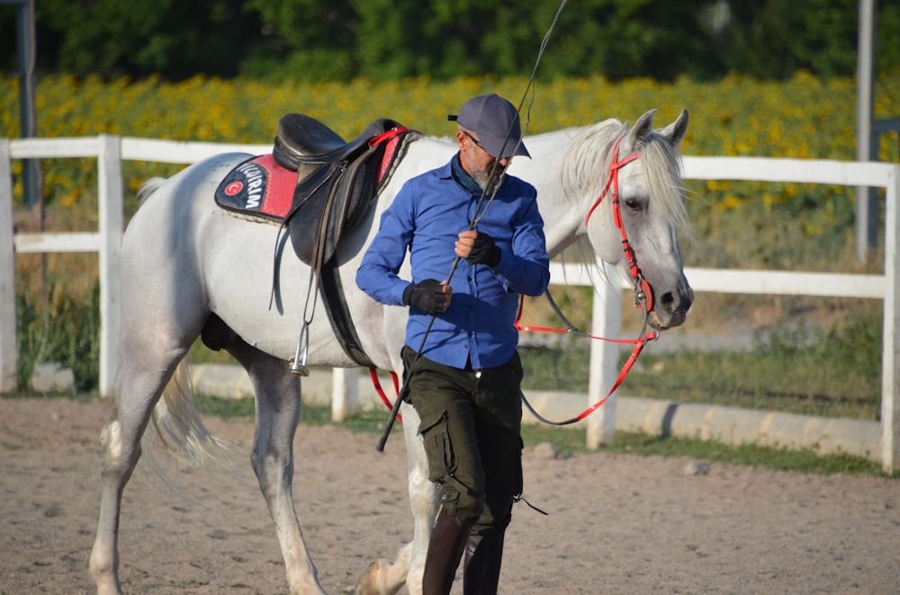 a man in blue jacket leading a white horse