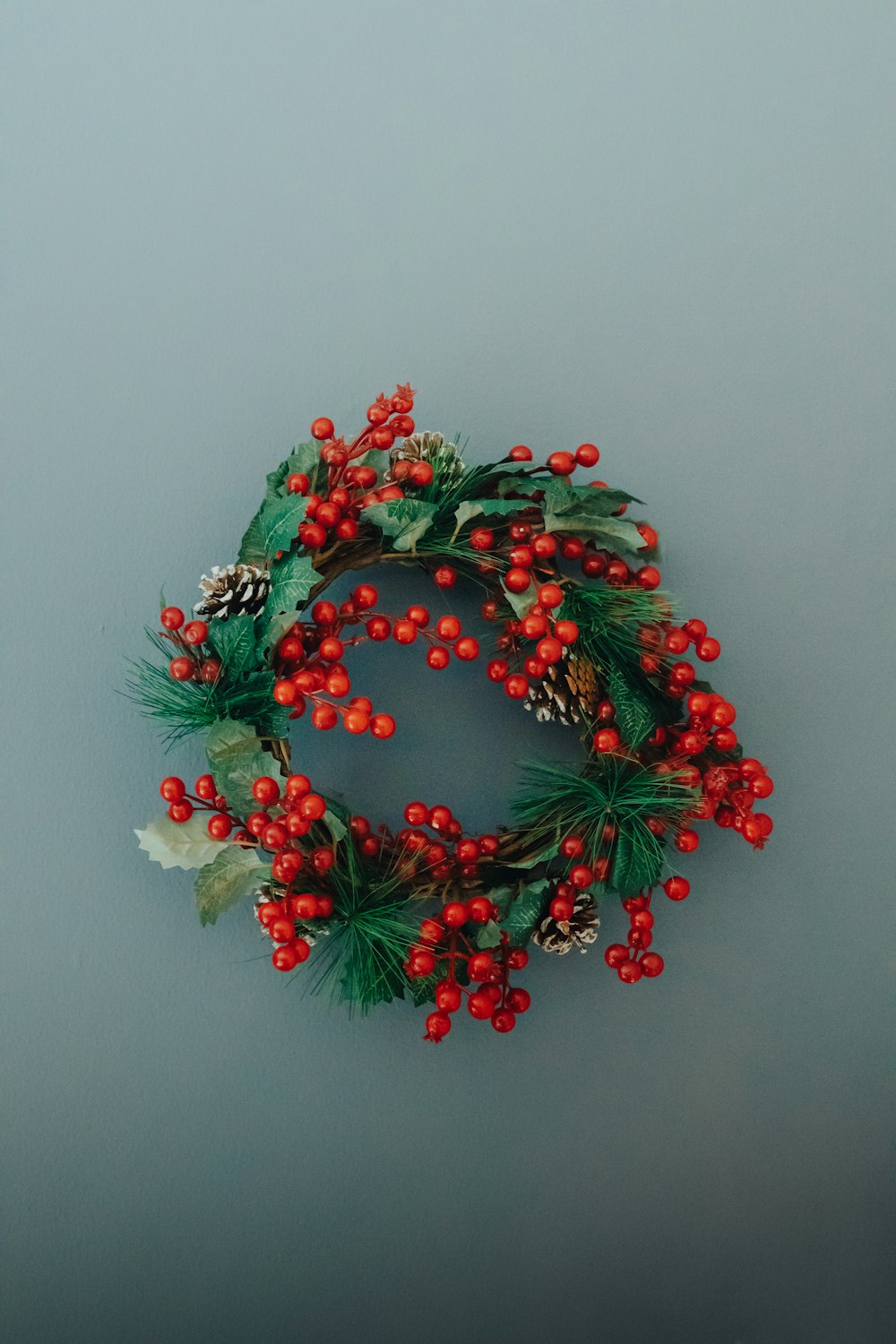 a christmas wreath with red berries and pine cones