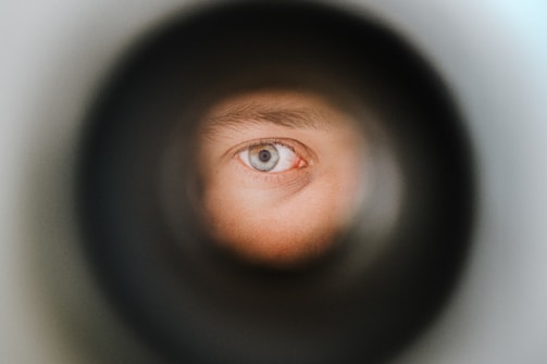 A close-up view of a person's eye as seen through a circular opening, with a sharp focus on the blue iris and details of the eyebrow and eyelid visible.