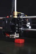 Detailed view of a 3D printer creating a miniature sailing yacht hull in white filament