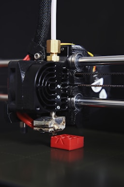 A close-up of a 3D printer nozzle carefully layering vibrant plastic to create a small mechanical part.