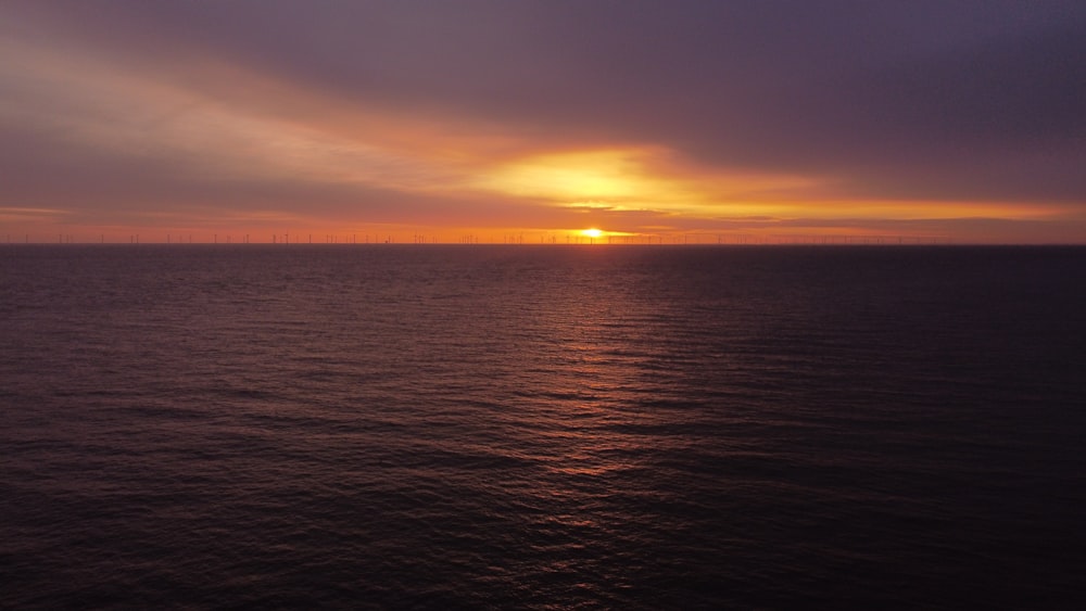 the sun is setting over the ocean on a cloudy day