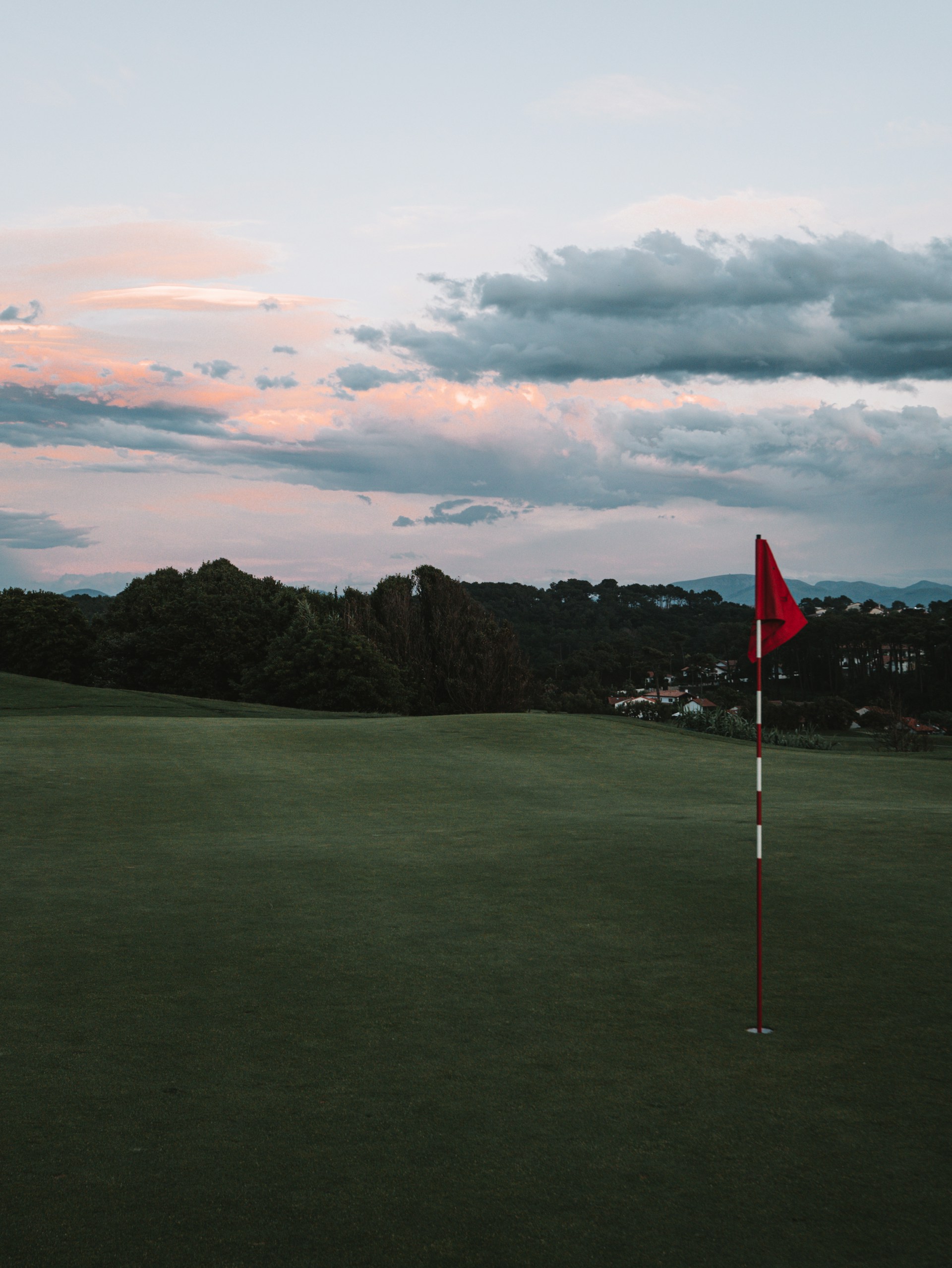 a red flag sticking out of the green of a golf course