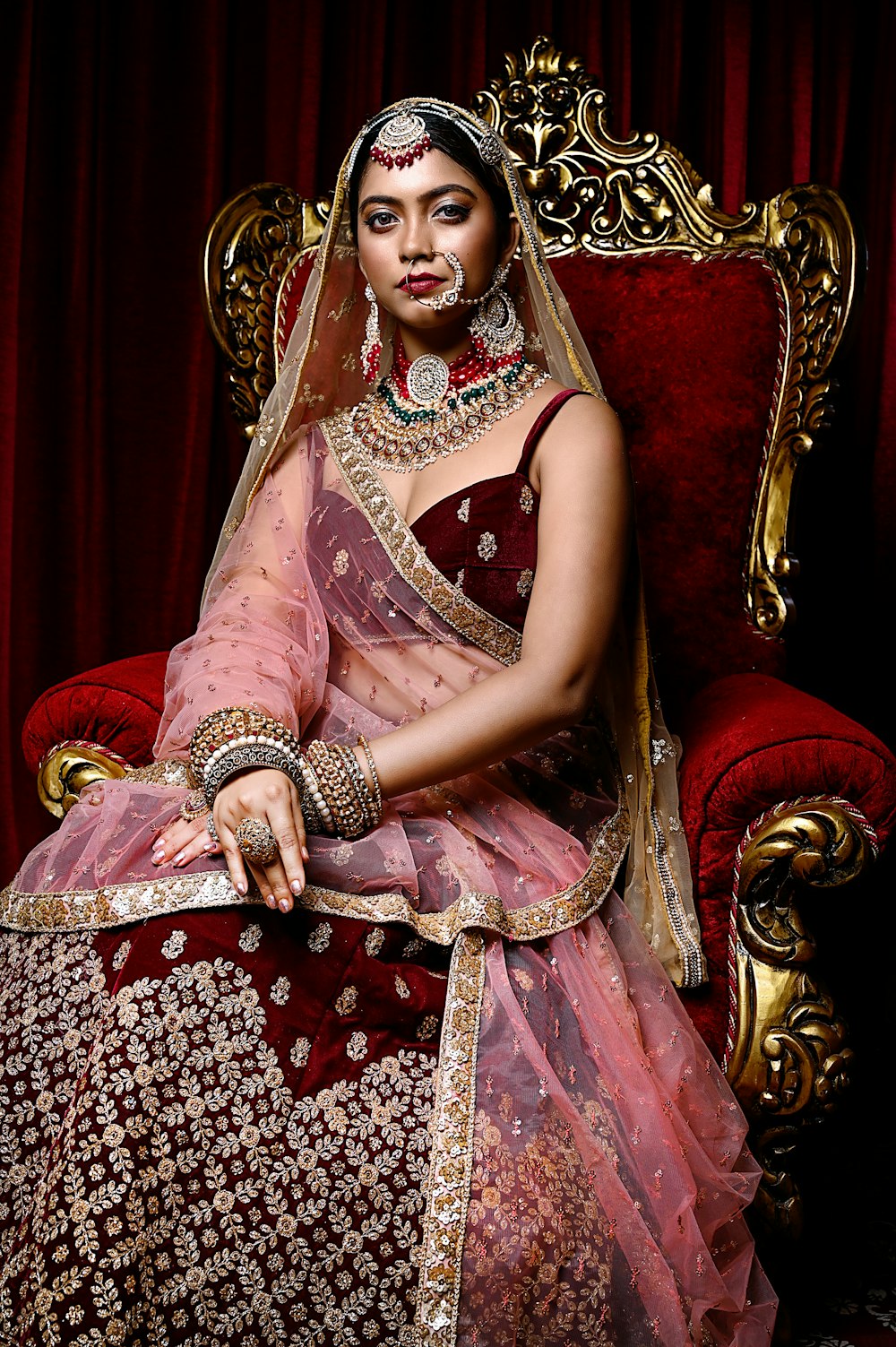 a woman in a red and gold bridal sitting on a red chair