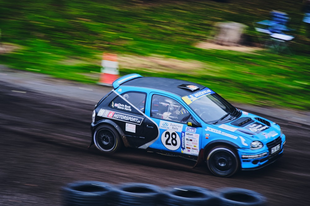 a small blue car driving down a dirt road