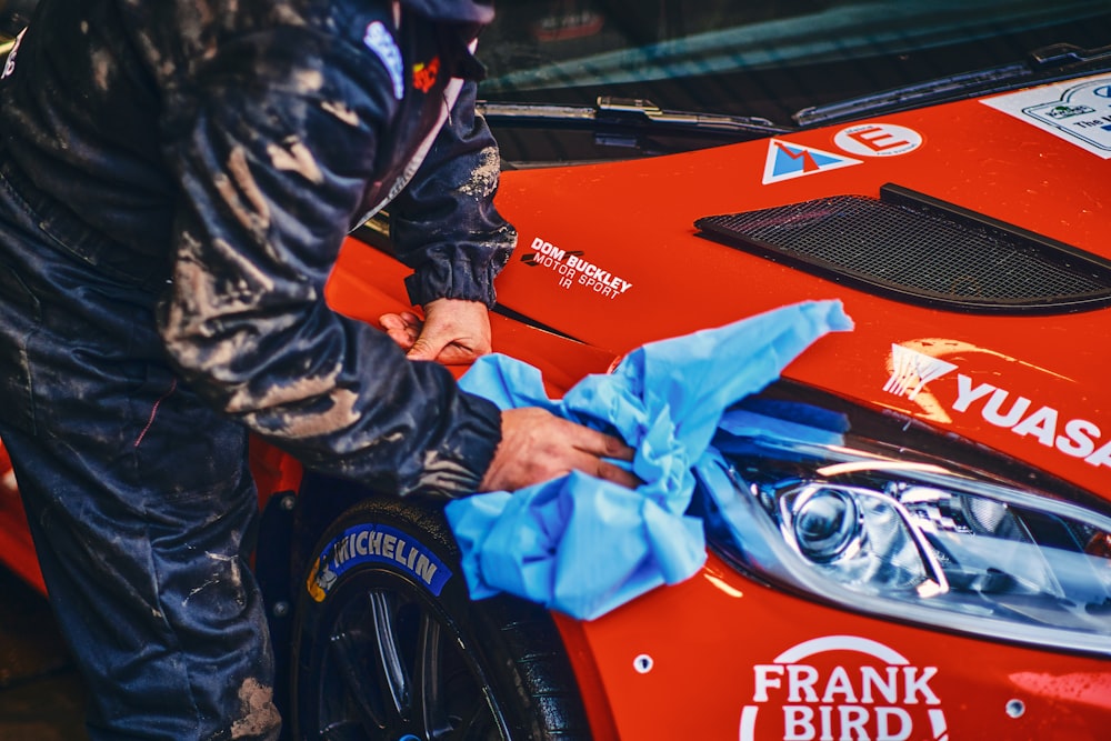 a man waxing the hood of a red sports car