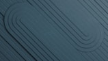 A geometric pattern featuring a series of parallel lines and rounded shapes embossed into a textured surface. The design emphasizes symmetry and balance, with the lines curving smoothly to form looped structures.