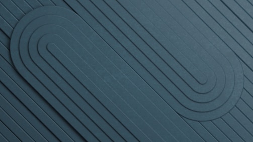 A geometric pattern featuring a series of parallel lines and rounded shapes embossed into a textured surface. The design emphasizes symmetry and balance, with the lines curving smoothly to form looped structures.